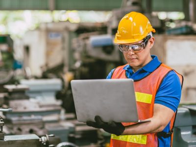 Asian male engineer worker happy using Laptop computer in heavy metal factory background.