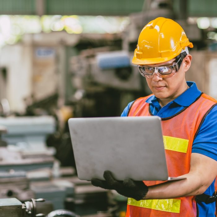 Asian male engineer worker happy using Laptop computer in heavy metal factory background.