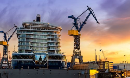 Scenic back view large modern luxury cruise ship liner under construction building cranes at dry dock shipyard in Hamburg port dramatic sunset sky background. Big vessel manufactoring site industry.