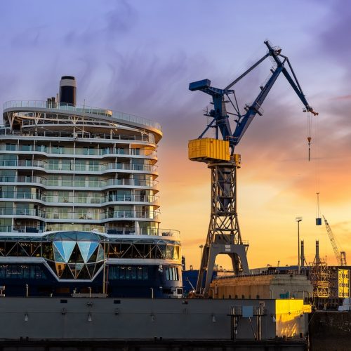 Scenic back view large modern luxury cruise ship liner under construction building cranes at dry dock shipyard in Hamburg port dramatic sunset sky background. Big vessel manufactoring site industry.